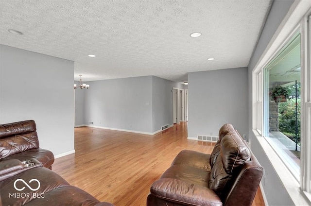 living room featuring an inviting chandelier, baseboards, visible vents, and light wood finished floors