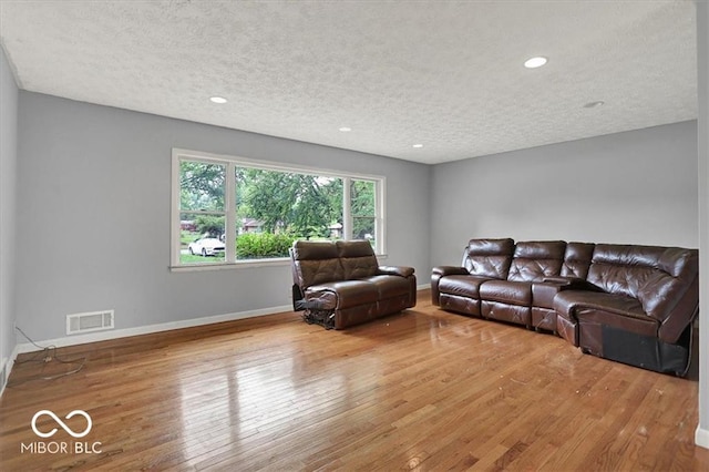 living room featuring visible vents, baseboards, a textured ceiling, and hardwood / wood-style flooring