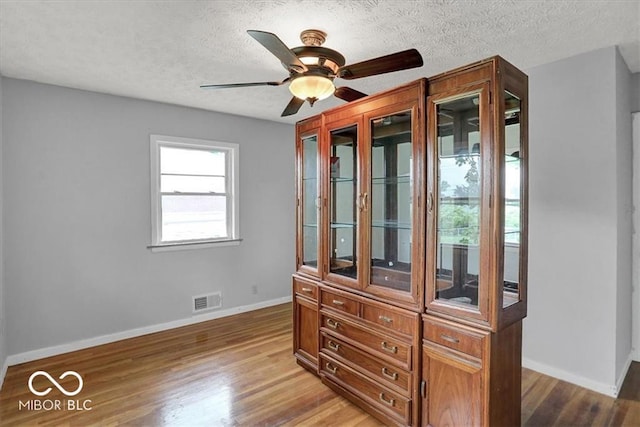 spare room featuring light wood finished floors, visible vents, baseboards, a textured ceiling, and a ceiling fan