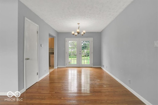 empty room featuring an inviting chandelier, wood finished floors, baseboards, and a textured ceiling