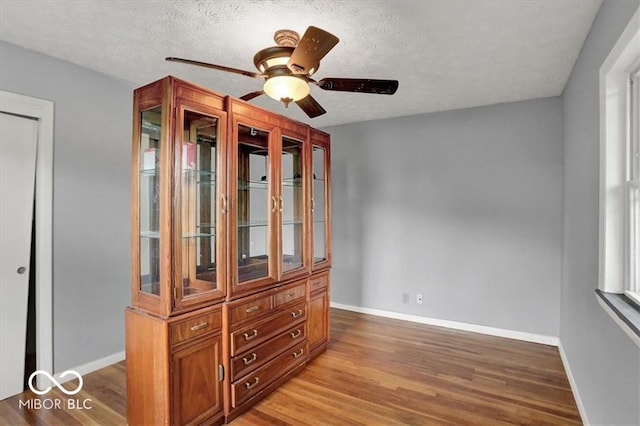 interior space featuring ceiling fan, wood finished floors, baseboards, and a textured ceiling