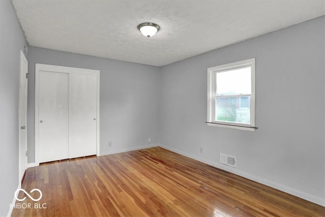 unfurnished bedroom with visible vents, a textured ceiling, wood finished floors, a closet, and baseboards