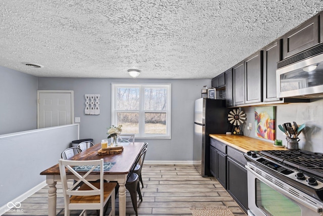 kitchen with light wood-type flooring, baseboards, appliances with stainless steel finishes, and a textured ceiling