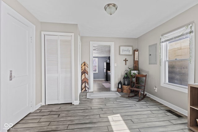 foyer entrance with baseboards, electric panel, visible vents, and wood finished floors