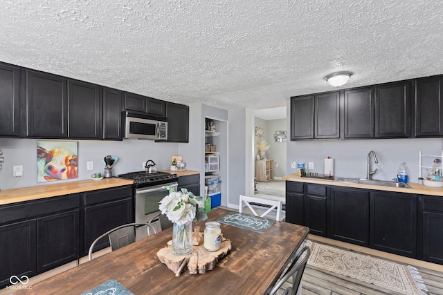 kitchen with butcher block counters, a textured ceiling, stainless steel appliances, and dark cabinetry