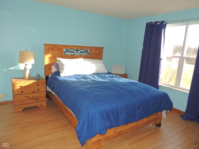 bedroom featuring baseboards, multiple windows, light wood-style floors, and a textured ceiling