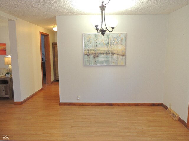 unfurnished dining area with visible vents, baseboards, a textured ceiling, and light wood-style flooring