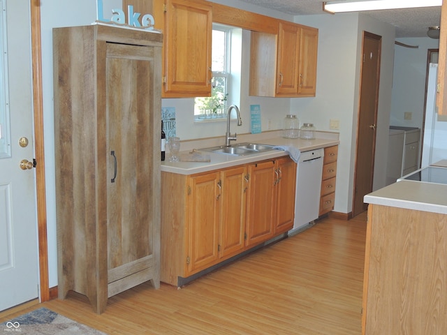 kitchen with light wood-style flooring, a sink, light countertops, dishwasher, and washing machine and dryer