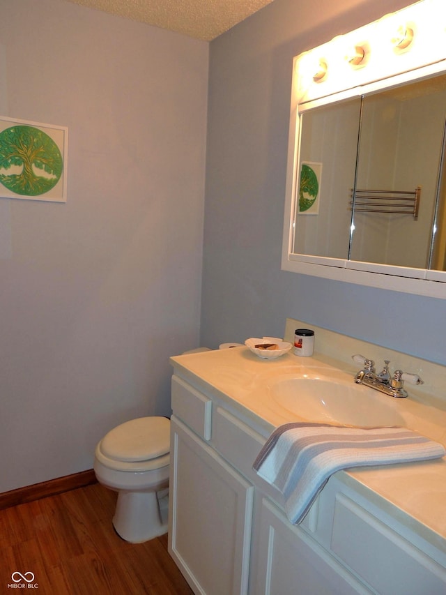 half bathroom featuring baseboards, toilet, vanity, wood finished floors, and a textured ceiling