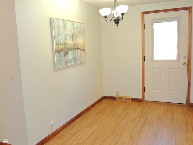 unfurnished dining area featuring baseboards, visible vents, an inviting chandelier, light wood-style flooring, and a textured ceiling