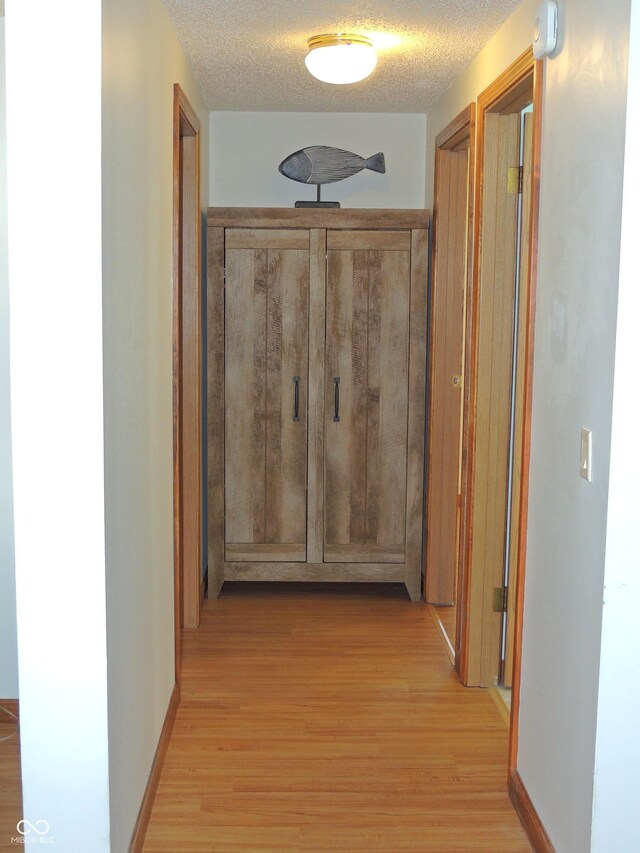 corridor with baseboards, light wood-type flooring, and a textured ceiling