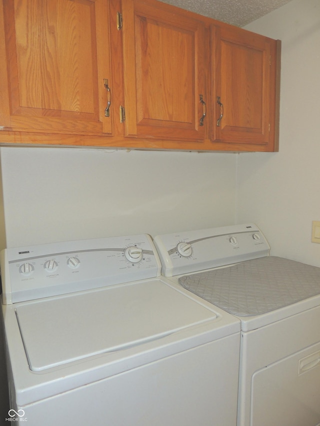 clothes washing area featuring cabinet space, a textured ceiling, and washing machine and clothes dryer