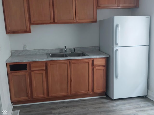 kitchen featuring light countertops, brown cabinetry, a sink, and freestanding refrigerator