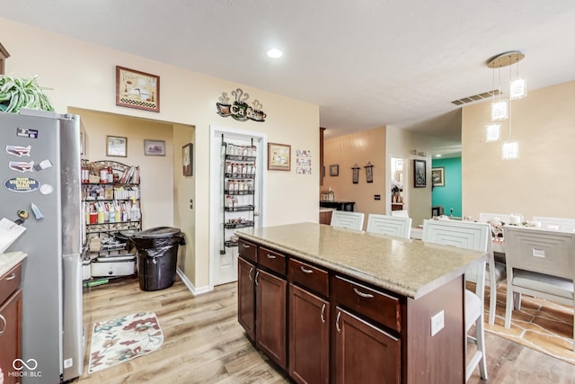 kitchen featuring visible vents, a breakfast bar area, freestanding refrigerator, and light wood-style floors