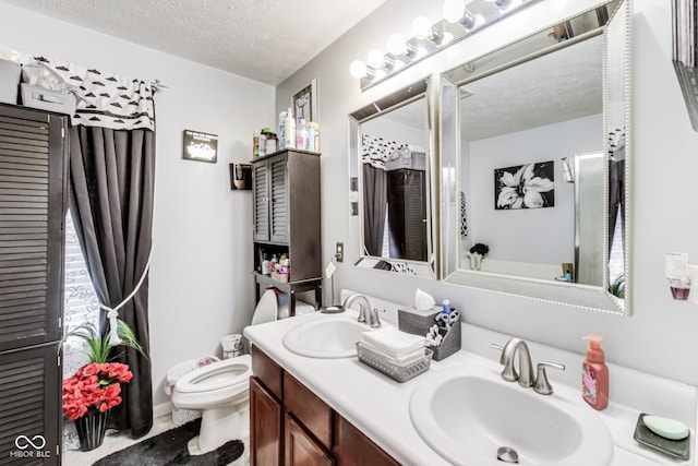 full bath with toilet, double vanity, a textured ceiling, and a sink