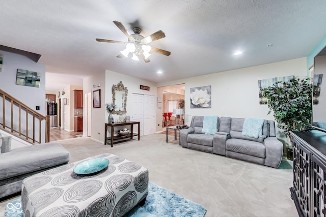 living area featuring ceiling fan, a textured ceiling, carpet flooring, baseboards, and stairway