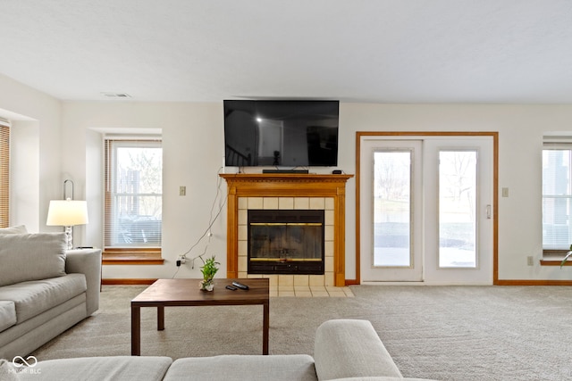 carpeted living area featuring baseboards, a fireplace, visible vents, and a healthy amount of sunlight