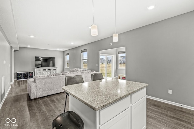 kitchen with a center island, dark wood-style flooring, white cabinetry, light stone countertops, and baseboards