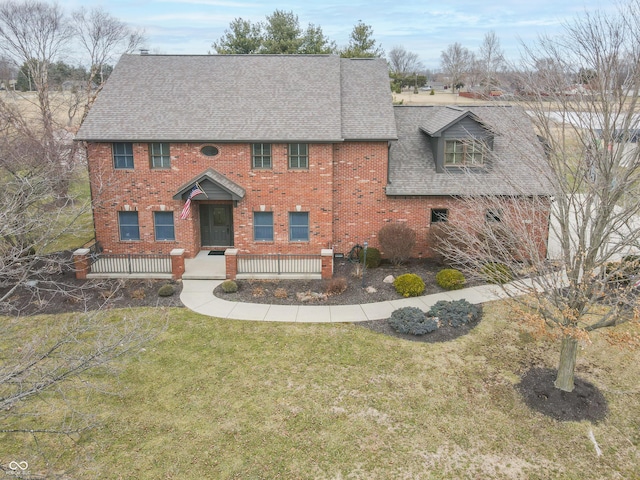 view of front facade featuring a front yard, brick siding, and roof with shingles