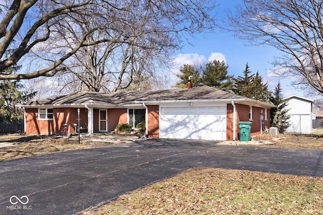 ranch-style home with aphalt driveway, brick siding, a chimney, and an attached garage