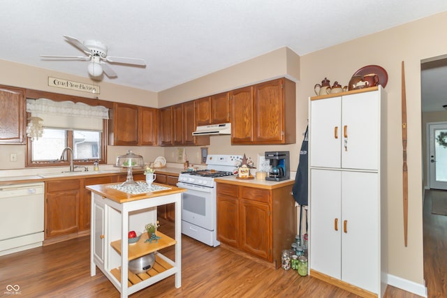 kitchen with under cabinet range hood, white appliances, wood finished floors, and a sink