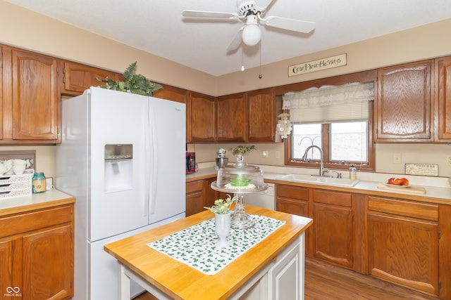 kitchen featuring a ceiling fan, wood finished floors, brown cabinetry, a sink, and white refrigerator with ice dispenser