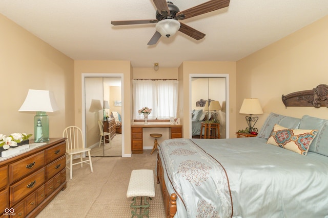 bedroom featuring light colored carpet, baseboards, multiple closets, and a ceiling fan