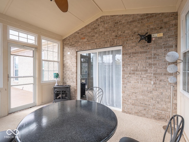 dining space featuring lofted ceiling, carpet floors, brick wall, and a wood stove