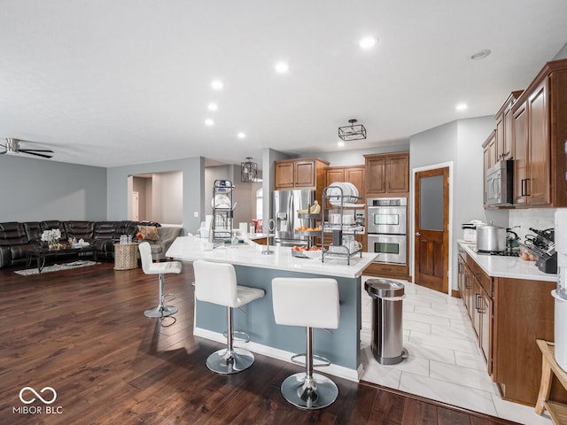 kitchen with appliances with stainless steel finishes, a breakfast bar, open floor plan, a large island with sink, and light wood-style floors