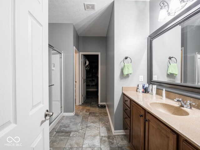 bathroom with a textured ceiling, vanity, visible vents, a spacious closet, and a stall shower