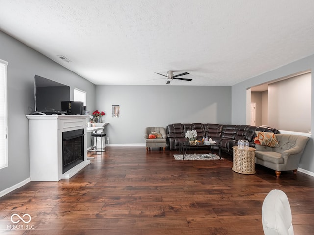 living room with a ceiling fan, a fireplace, visible vents, and wood finished floors