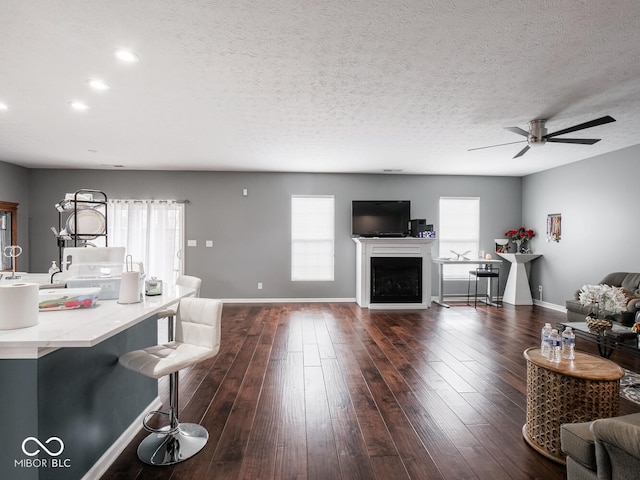 living room featuring a textured ceiling, dark wood-type flooring, a fireplace, and baseboards