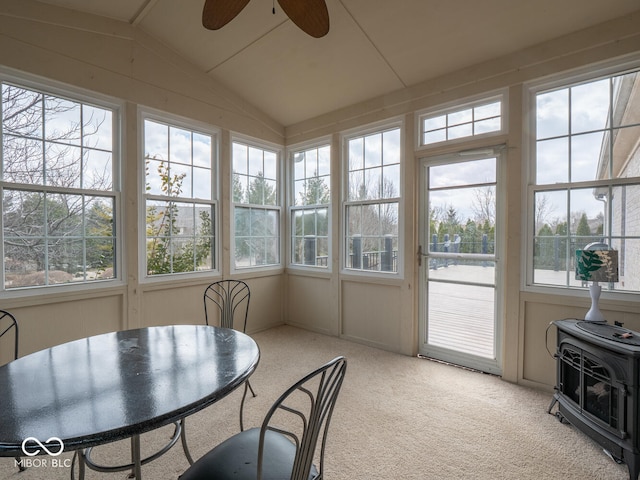 sunroom featuring a wood stove, a ceiling fan, vaulted ceiling, and a wealth of natural light