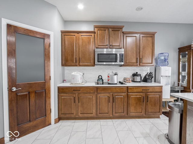 kitchen featuring light countertops, tasteful backsplash, stainless steel microwave, and brown cabinetry