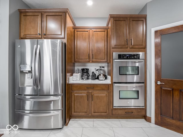 kitchen featuring appliances with stainless steel finishes, light countertops, marble finish floor, and brown cabinets