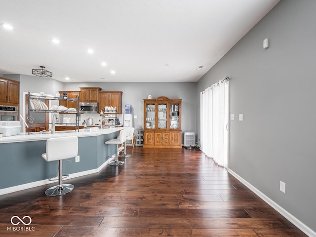 kitchen with stainless steel appliances, recessed lighting, brown cabinetry, dark wood-type flooring, and a kitchen breakfast bar