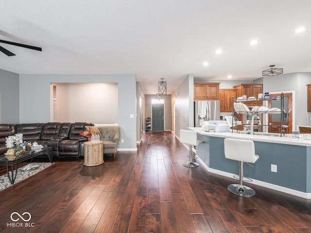 kitchen with stainless steel fridge, a ceiling fan, a breakfast bar area, open floor plan, and dark wood-type flooring