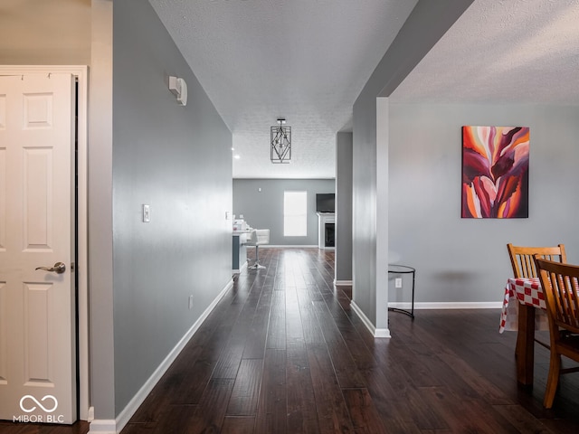 hall featuring dark wood-style flooring, a textured ceiling, and baseboards