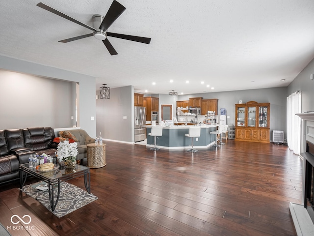 living area featuring a textured ceiling, dark wood-style flooring, a fireplace, a ceiling fan, and baseboards