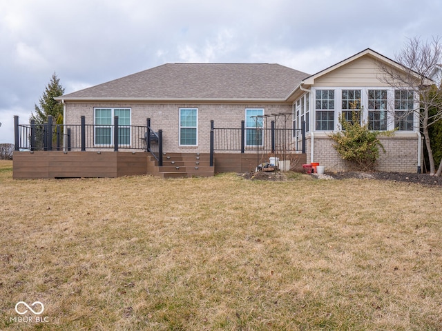 view of front of property with a shingled roof, brick siding, a wooden deck, and a front lawn