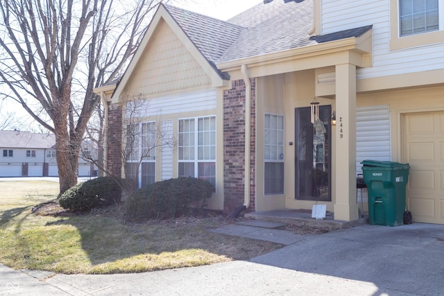 property entrance featuring a garage, brick siding, driveway, and a shingled roof