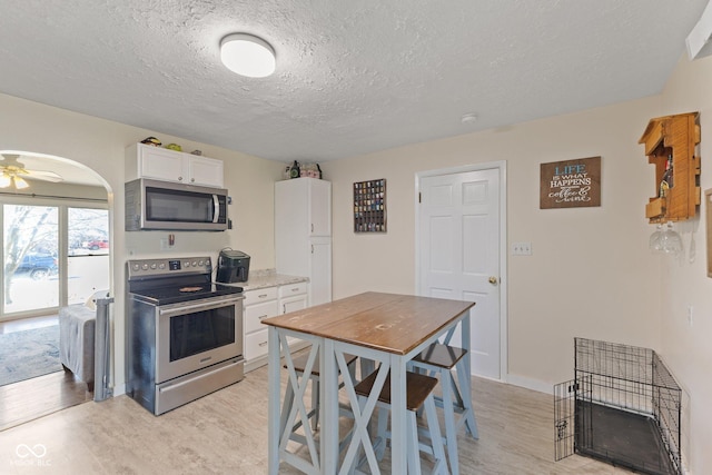 kitchen with light wood finished floors, stainless steel appliances, light countertops, white cabinetry, and ceiling fan