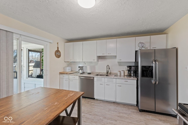 kitchen with stainless steel appliances, light countertops, light wood-type flooring, white cabinetry, and a sink