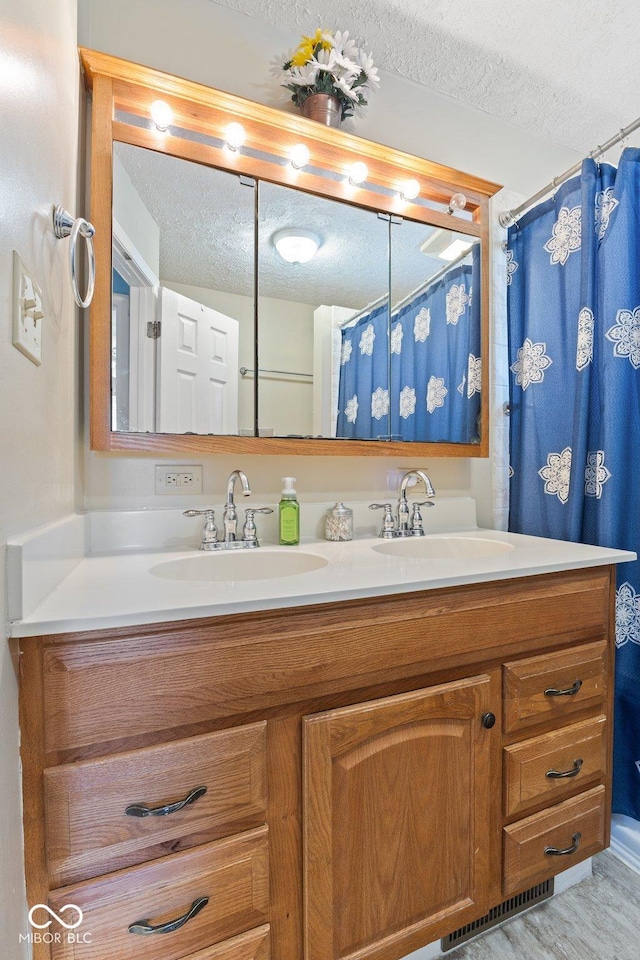 full bath with visible vents, a sink, a textured ceiling, and double vanity