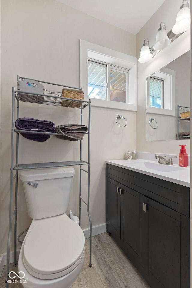 half bath featuring plenty of natural light, vanity, toilet, and wood finished floors