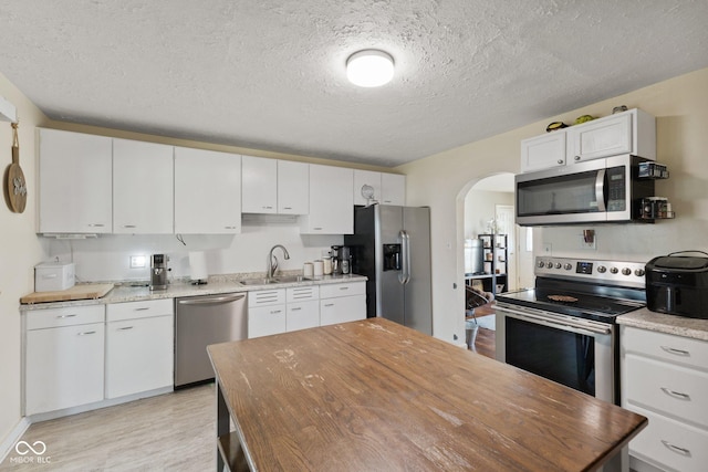 kitchen with stainless steel appliances, arched walkways, white cabinetry, and a sink