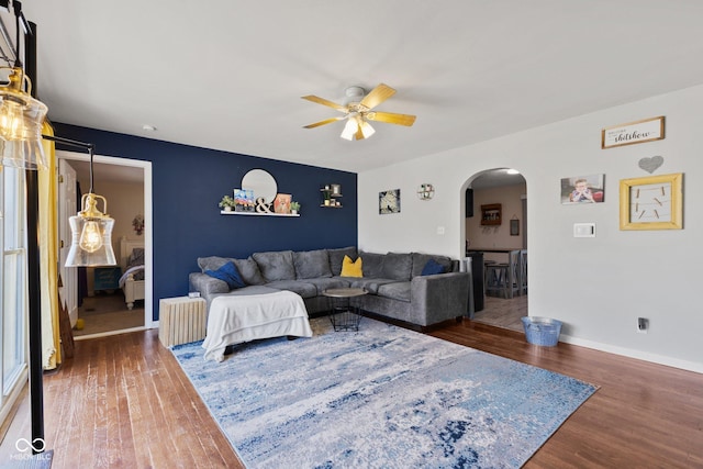 living room featuring a ceiling fan, arched walkways, baseboards, and wood finished floors