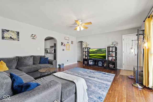 living room with baseboards, ceiling fan, arched walkways, and hardwood / wood-style floors