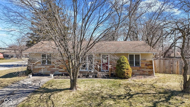 view of front facade with stone siding, fence, a front lawn, and roof with shingles