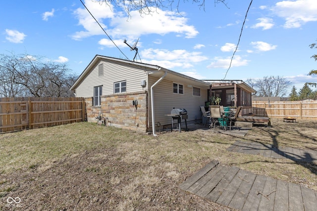 back of house featuring stone siding, a fenced backyard, and a yard